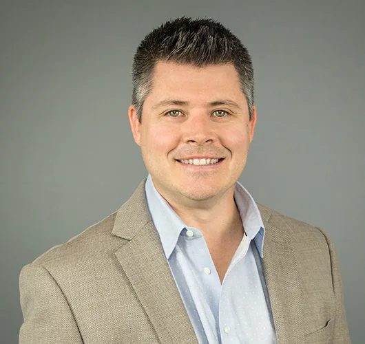 Headshot of Kurt Bialobreski wearing tan jacket over light blue button down shirt against light gray background