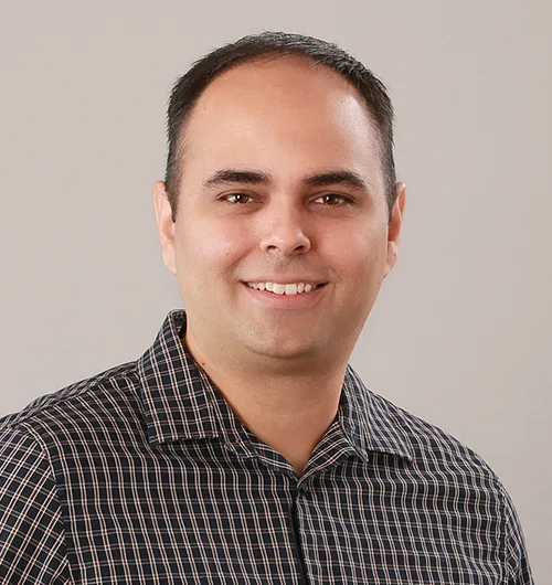 Headshot of Brian Maldonado on light beige background, wearing black and white checked shirt