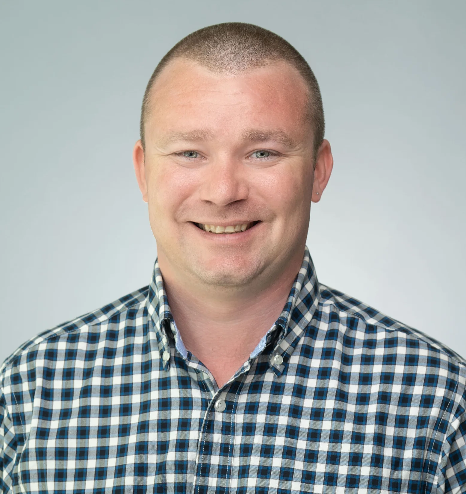 Portrait of Josh Gray wearing black, blue and white checked button down shirt on light gray background