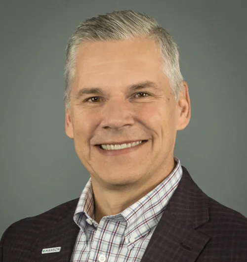 Headshot of Steve Donahue wearing maroon, gray and white checked button-down shirt under black checked jacket against medium-gray background