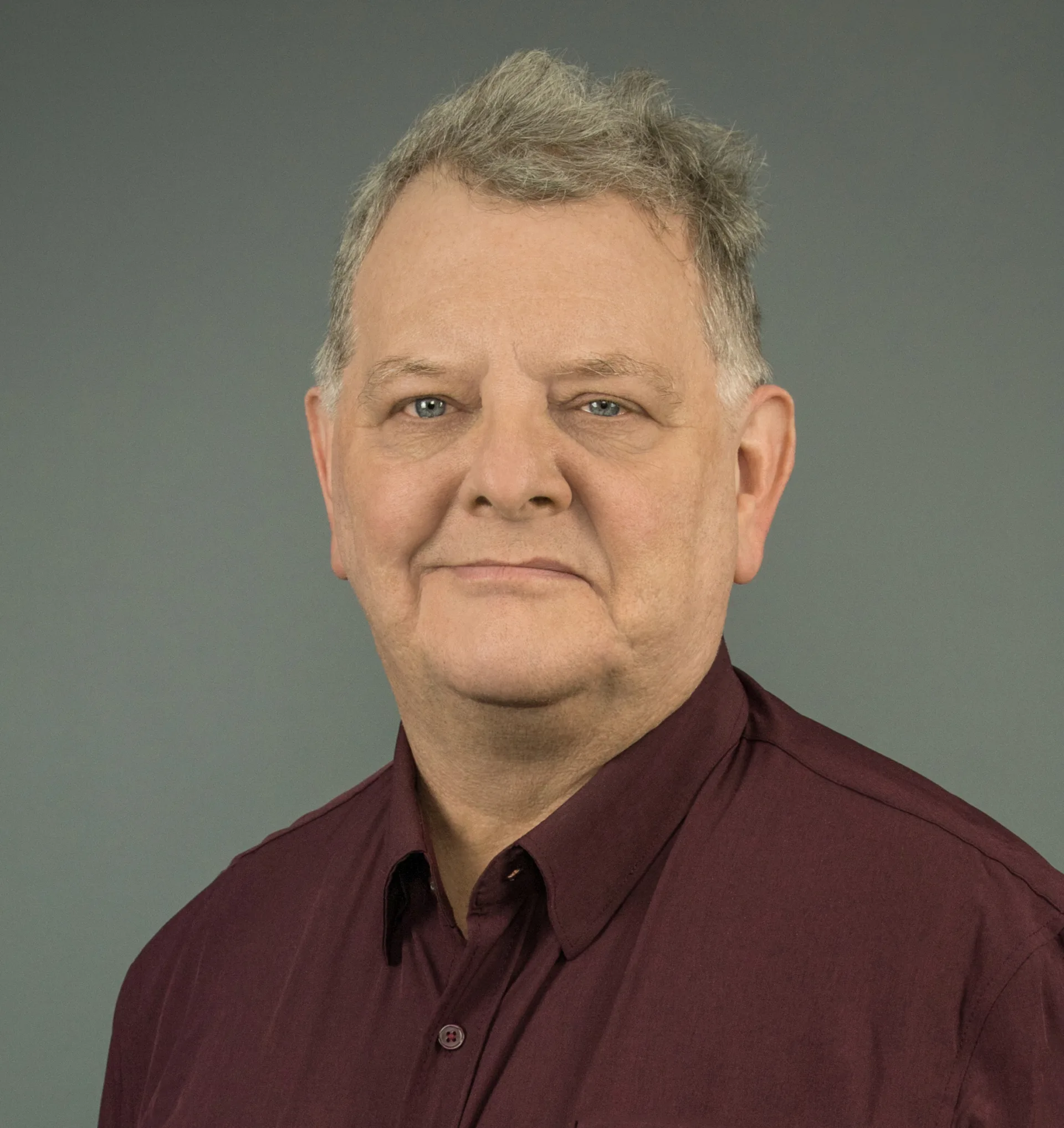 headshot of Ron Koons wearing maroon button-down shirt on gray background
