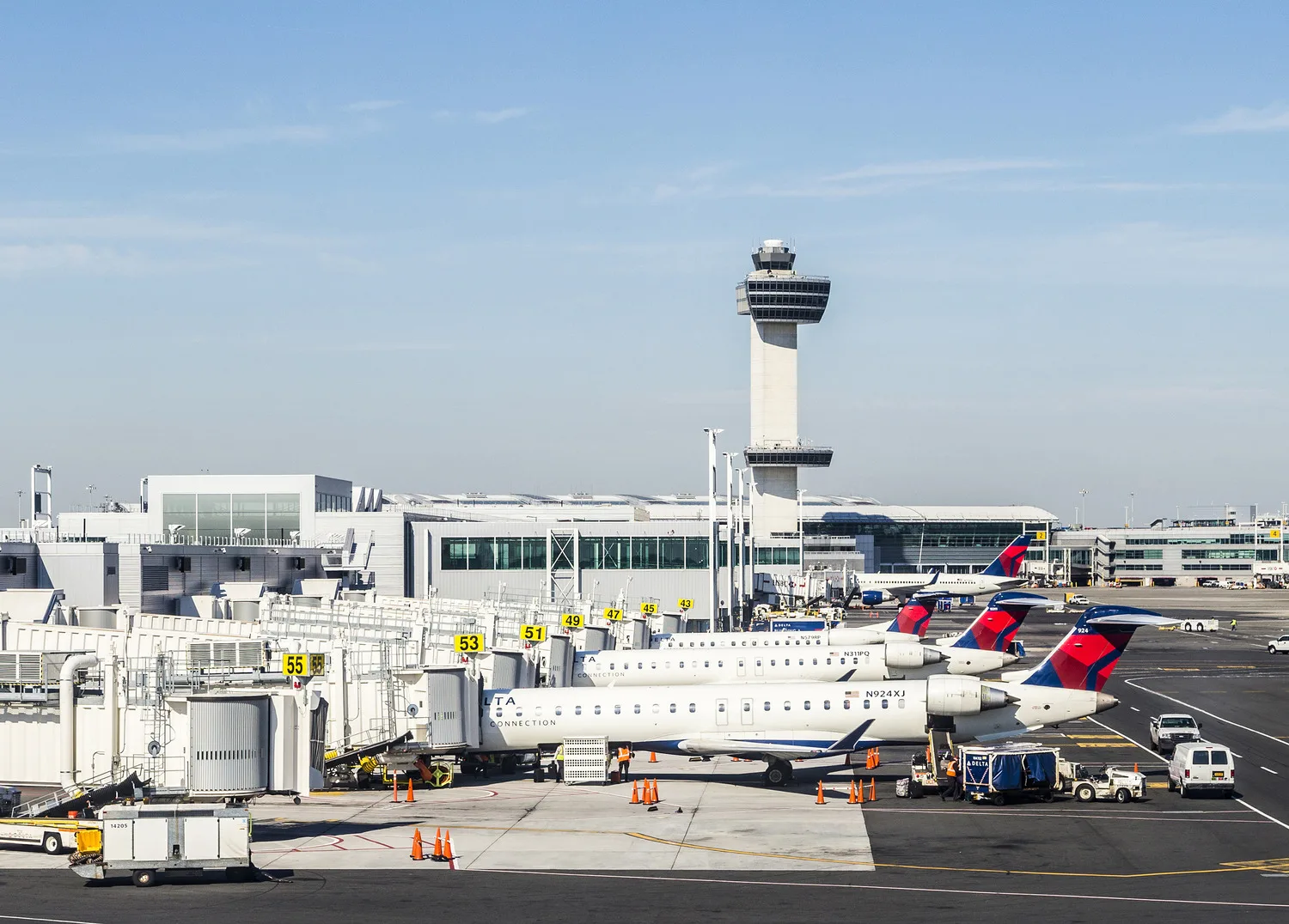 Exterior view of a large airport with planes lined up at gates and air-traffic control tower in background
