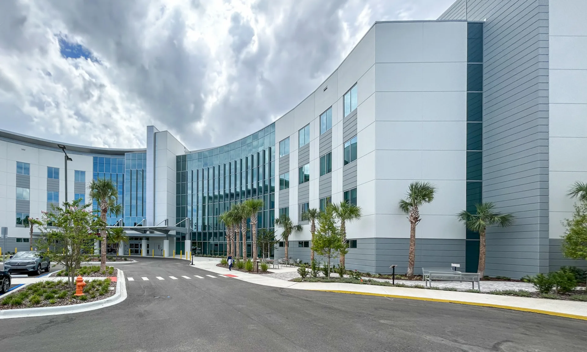 AdventHealth Palm Coast building exterior with palm trees in foreground, two cars at left in parking lot and white clouds in sky