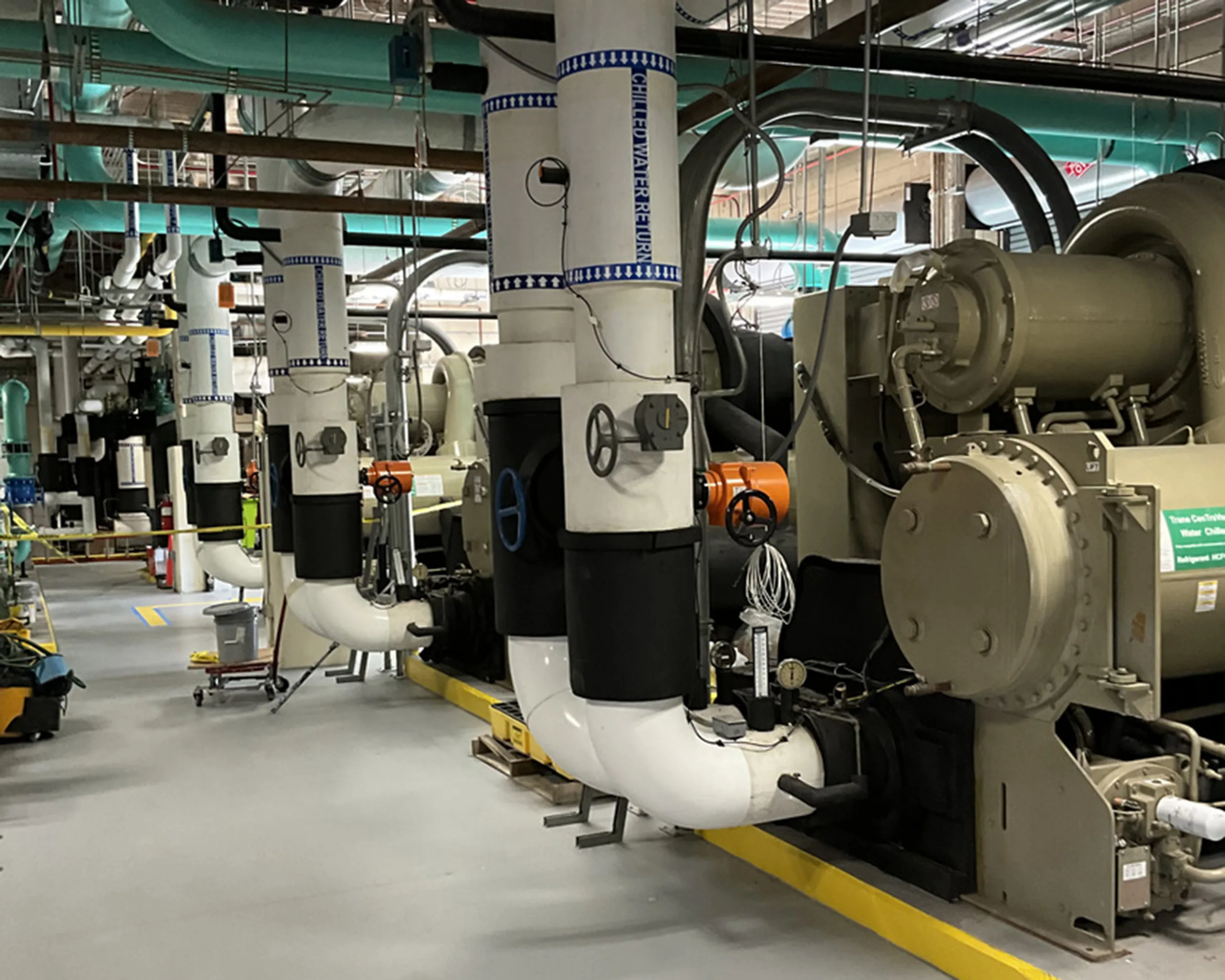 Photo inside mechanical room at Kissimmee hospital, with turquoise-colored pipes on ceiling and beige-colored equipment in foreground