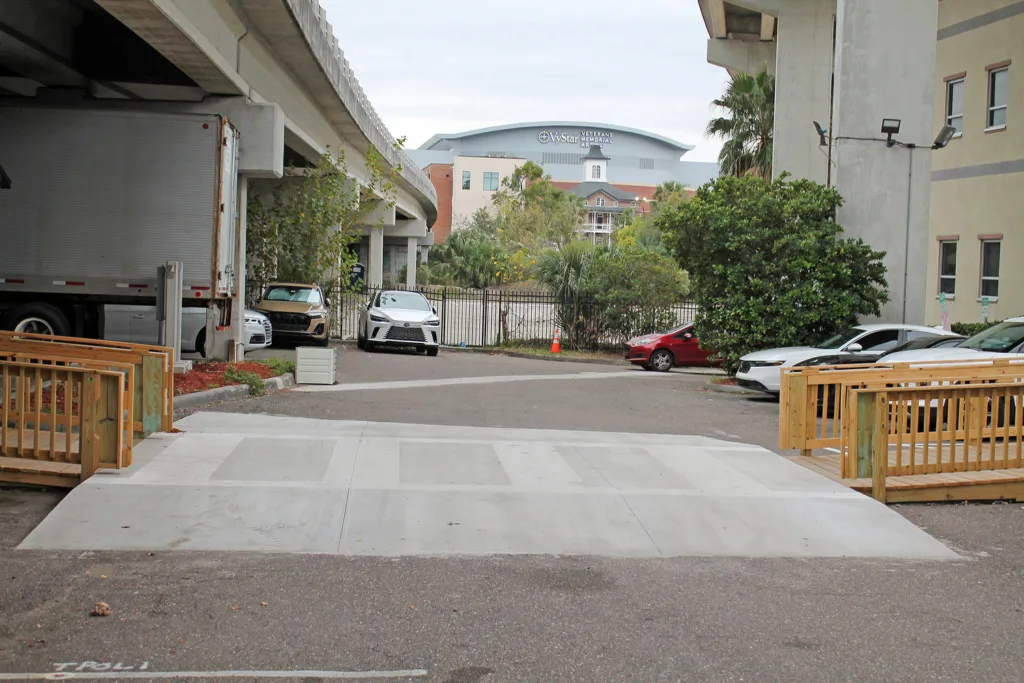Concrete pathway between two wooden ramps with trees, cars and buildings in background