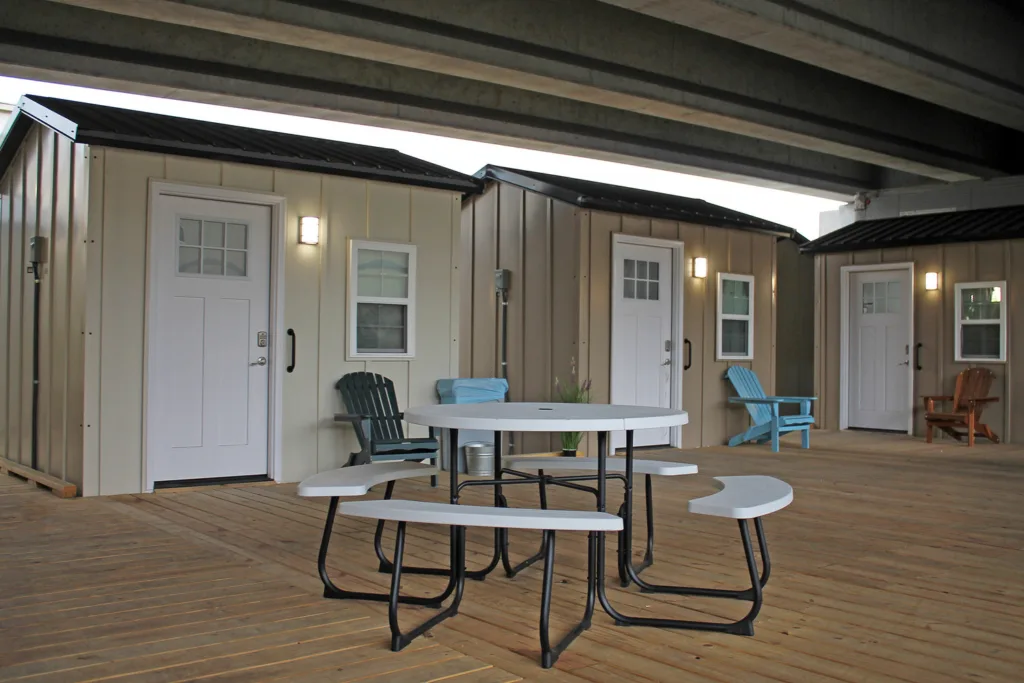 White picnic table in foreground and three small houses with white doors and white-framed windows in background