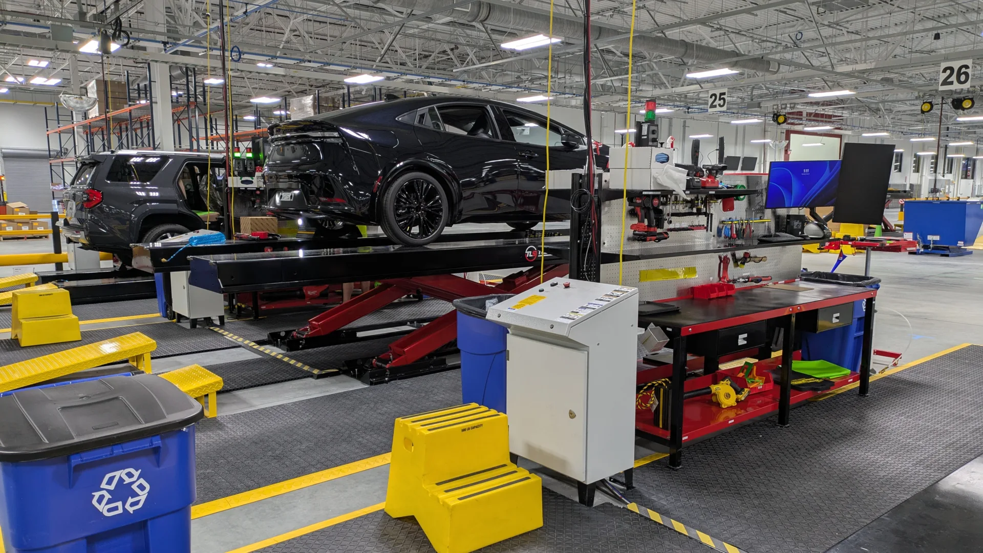 View of a black car in foreground and a gray SUV in background inside a vehicle servicing warehouse