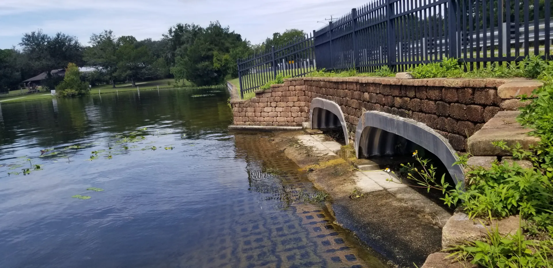 Ground-level view of a brick dam with water at left and a black fence at upper right