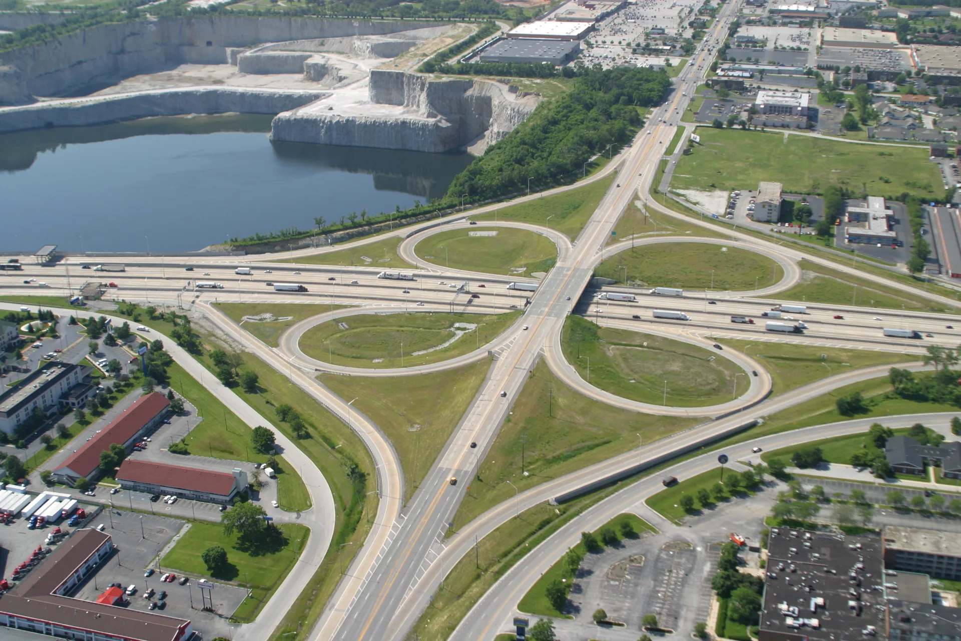 Aerial photo of a cloverleaf interchange with a quarry in the upper left corner and buildings and grass in remaining quadrants of photo