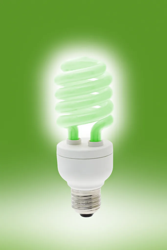 Glowing green light bulb on green background
