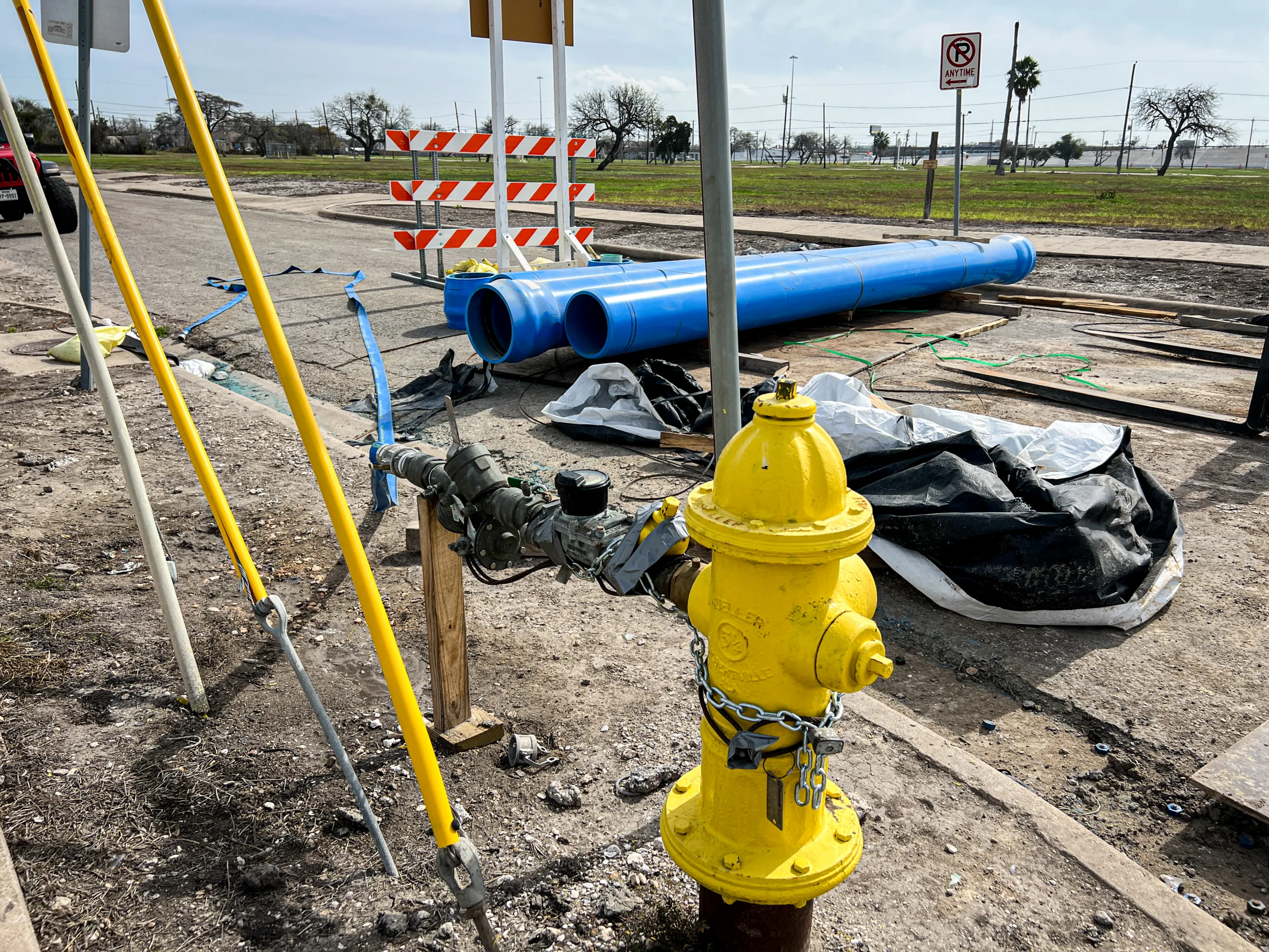 Ground-level image of road construction with sewer drainage equipment laid out behind road blockade; yellow fire hydrant in foreground