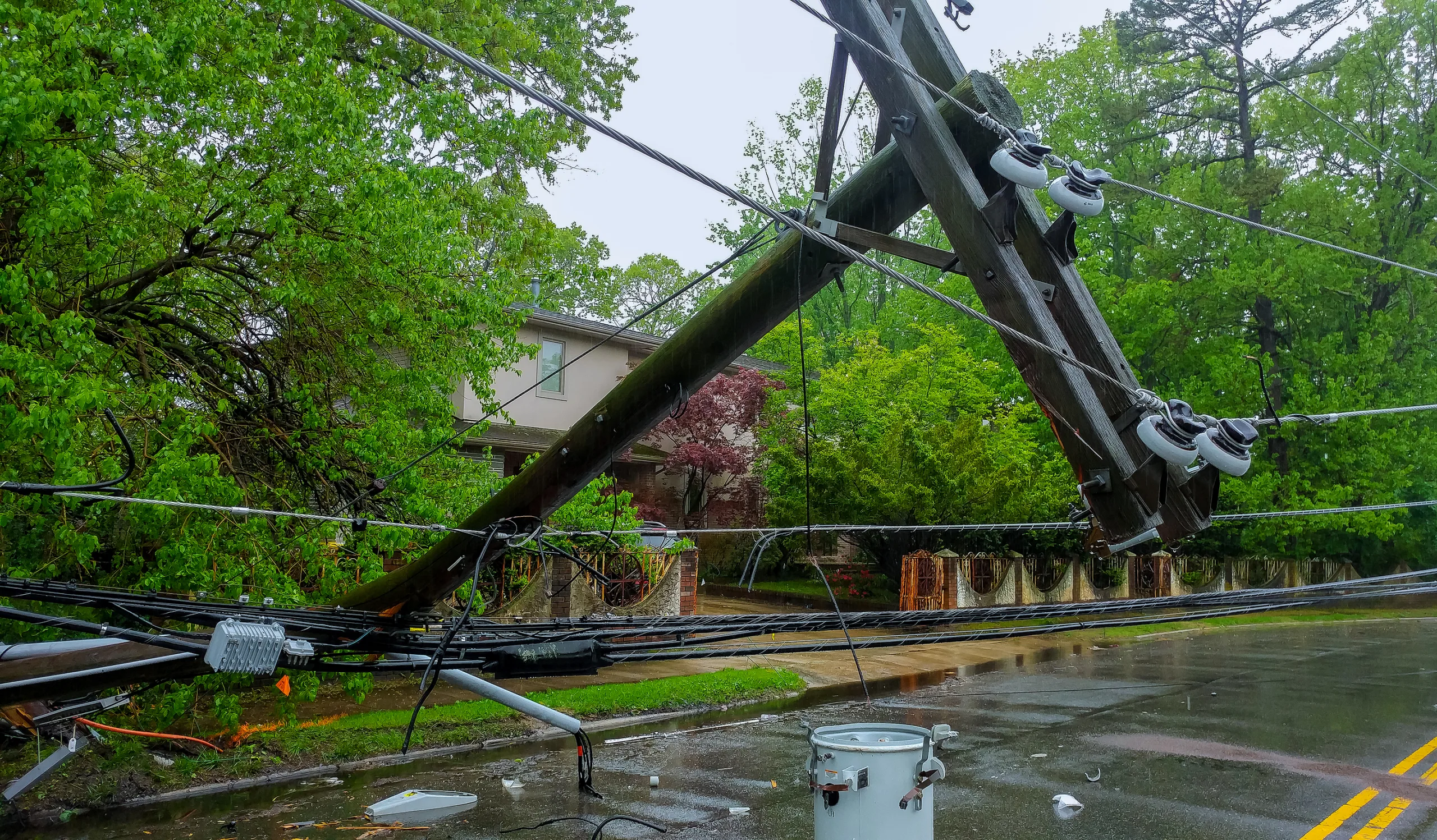 Downed power lines over a street with a house and green trees in the background